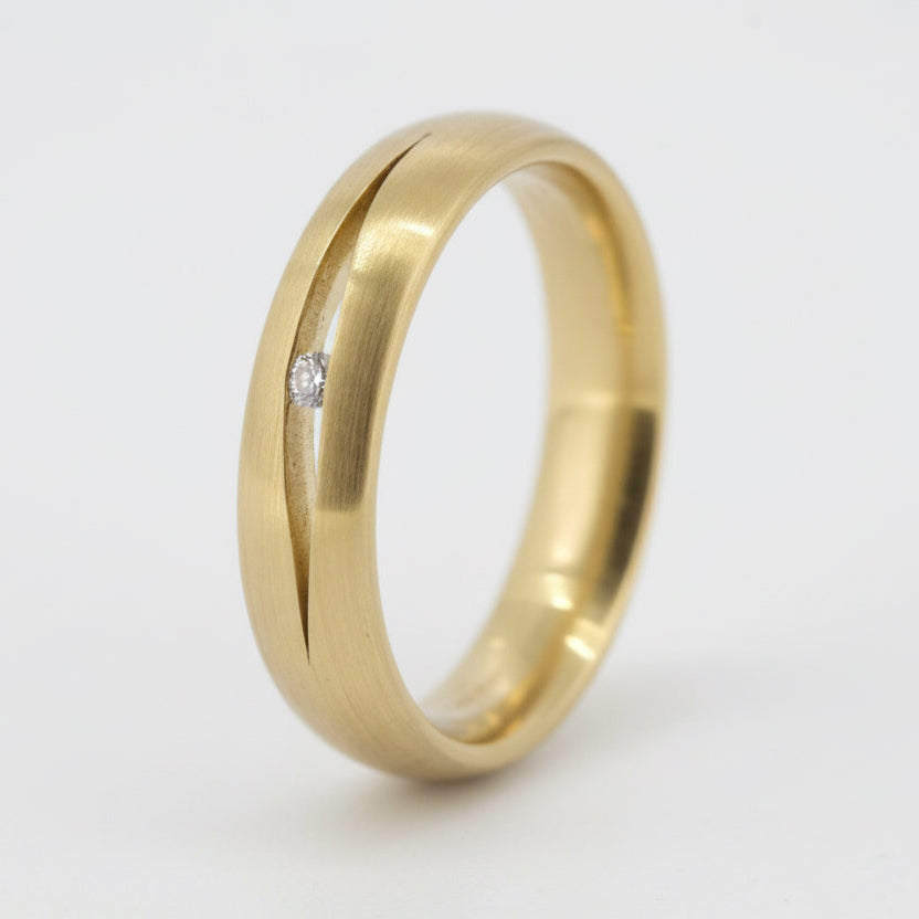A gold wedding band with a single diamond embedded on the inside edge, showing a shiny finish and a subtle width
