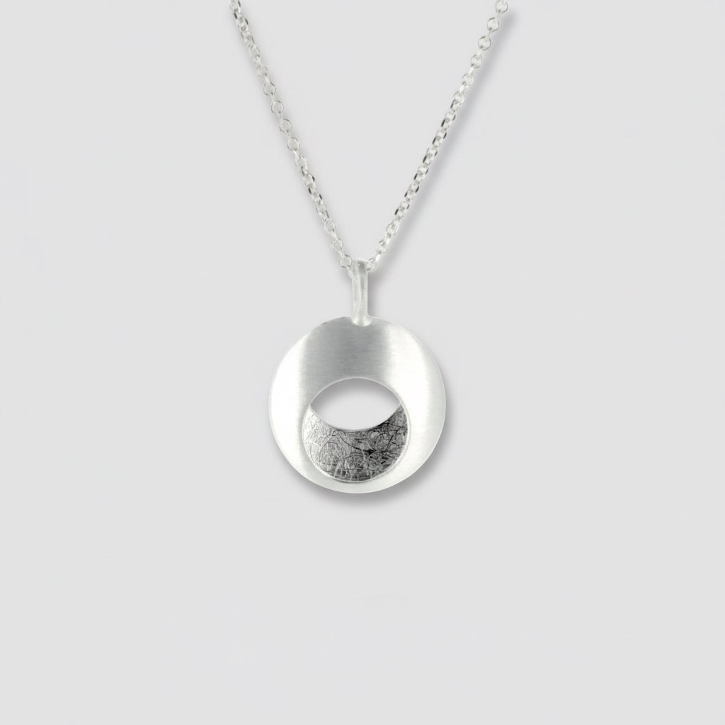 A sterling silver pendant in the shape of a circle with a textured center, displayed against a white background