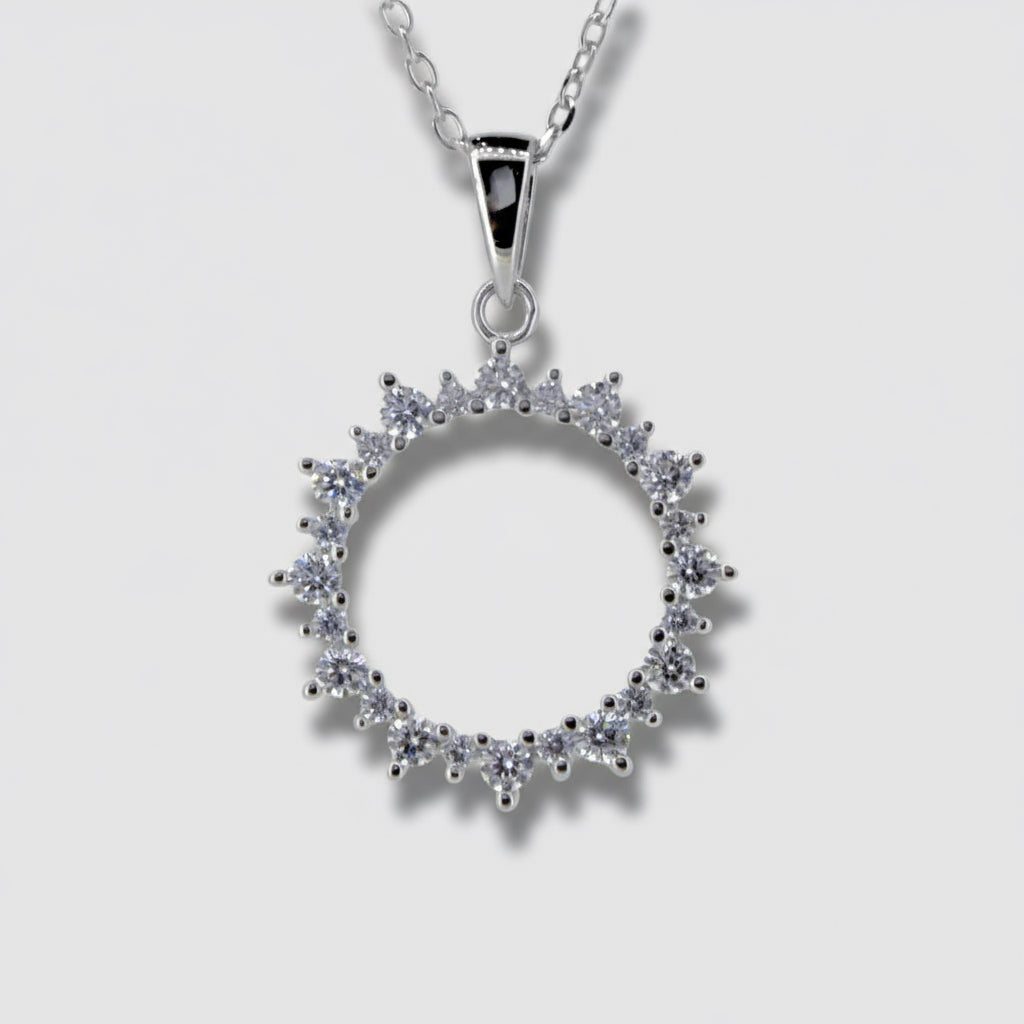 A silver-colored pendant featuring a circular design with cubic zirconia stones set within it, attached to a fine silver chain.