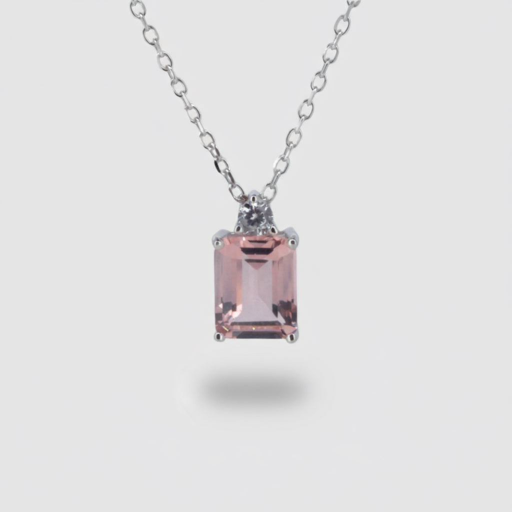 A silver and peach colored cubic zirconia pendant on a chain.
