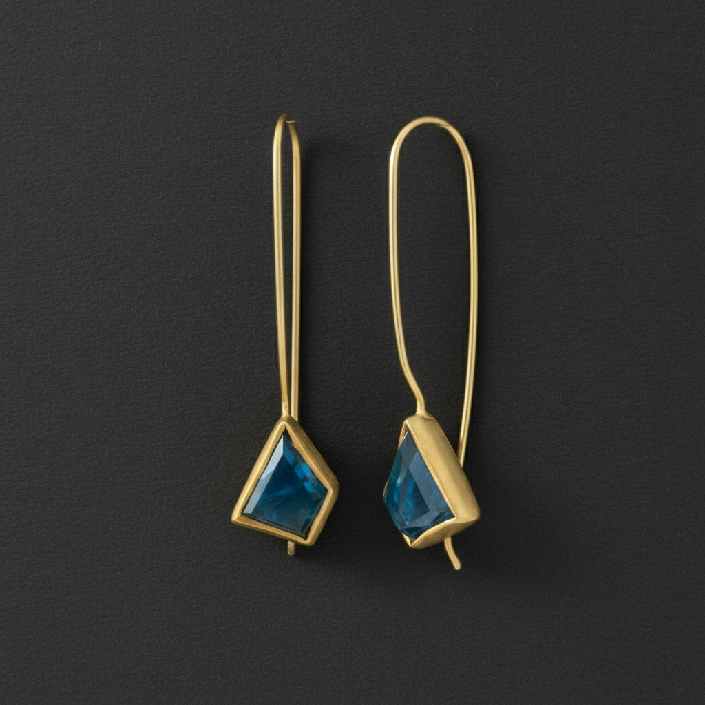 Pair of gold earrings with blue triangular stones on a white background
