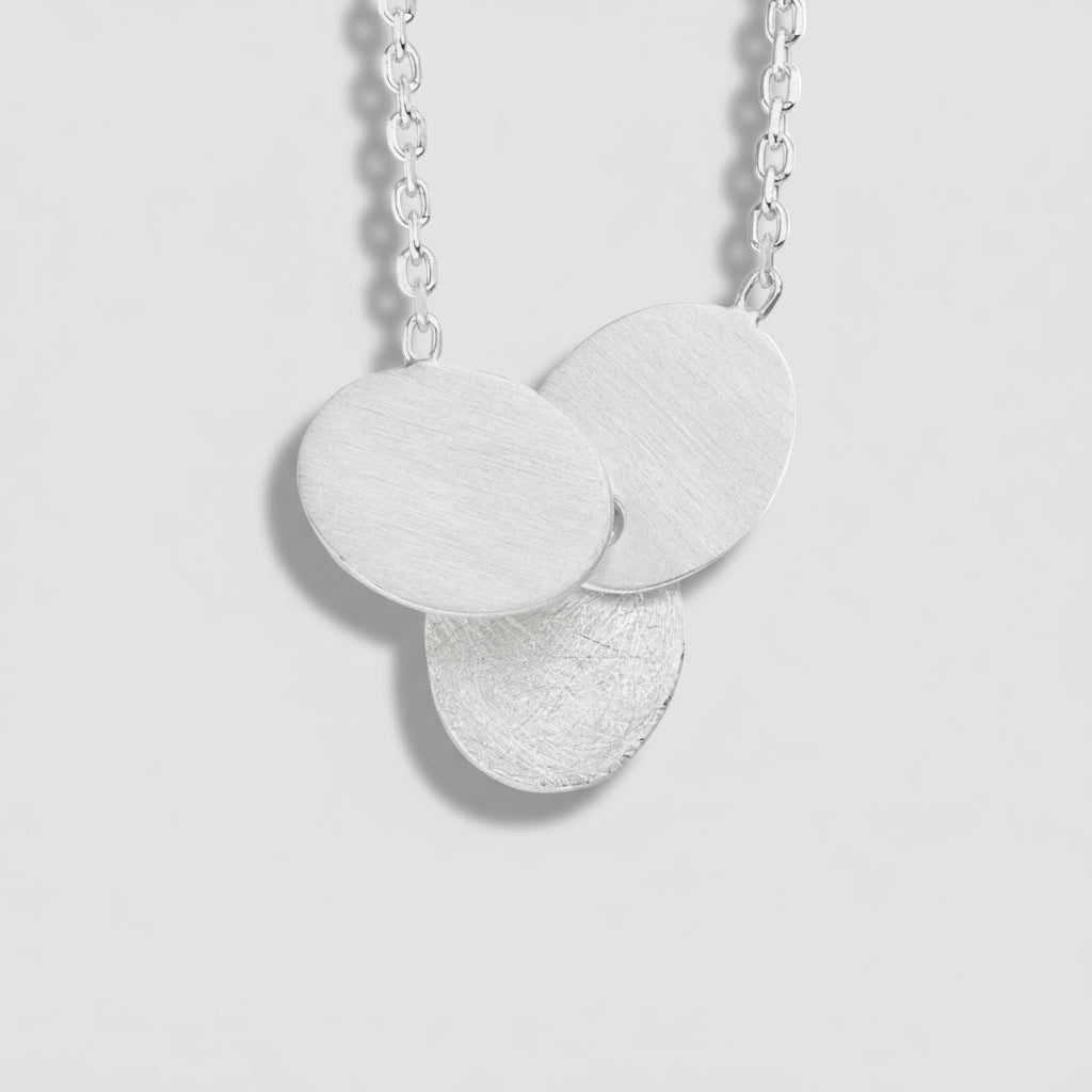 Silver necklace with three round pendants on a white background
