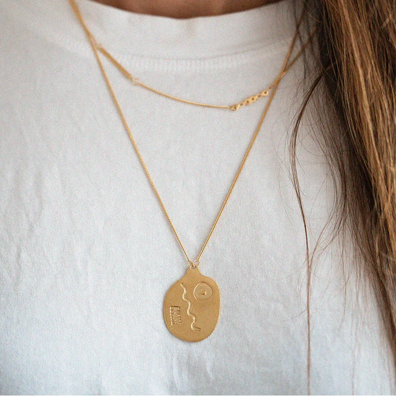 Close-up of a person wearing a gold necklace with a pendant on a white background