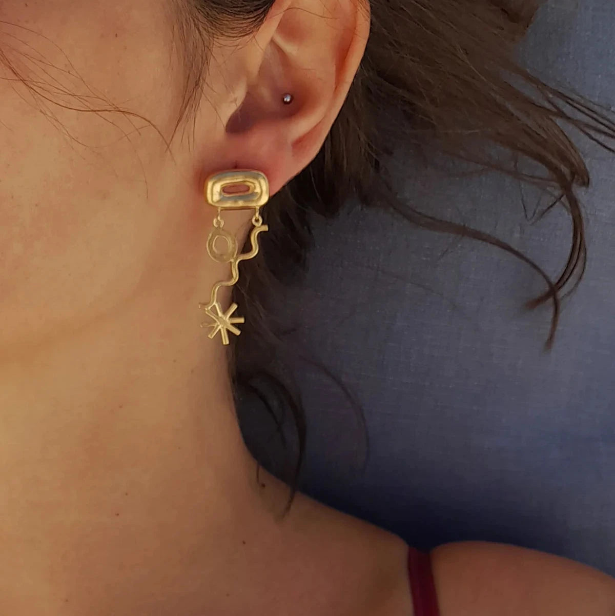 Close-up of a person wearing a gold earring with star and circle designs.