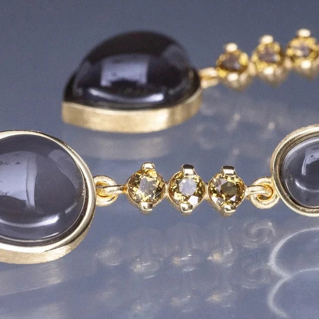 Gold earrings with dark gemstones on a reflective surface
