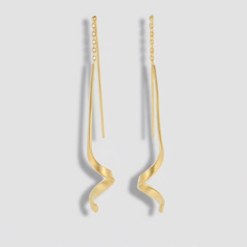Gold earrings with wavy design on a light gray background.