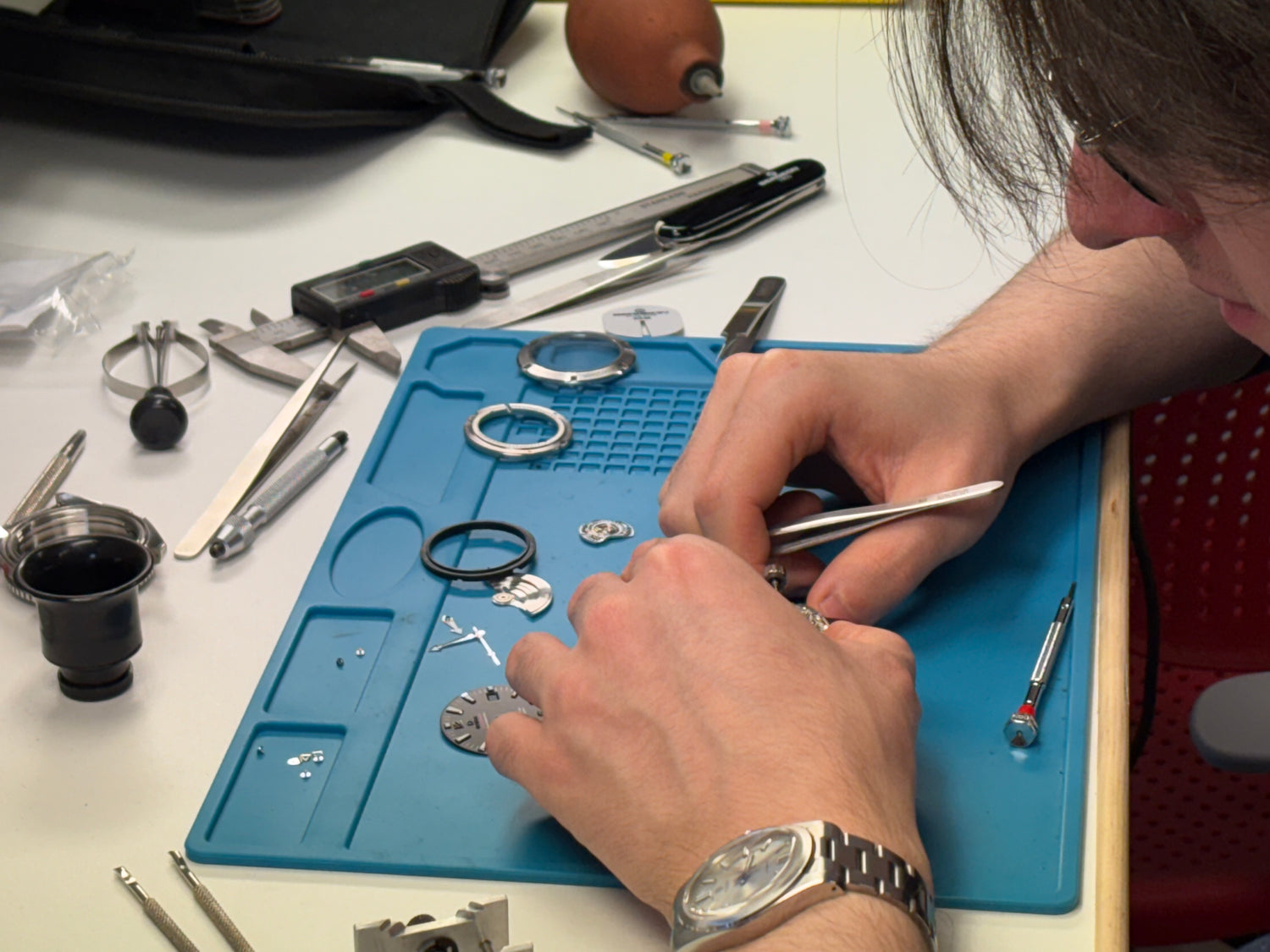 Person working on a small object with tools on a blue mat