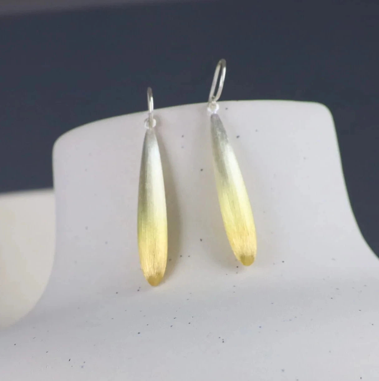 Gold teardrop earrings on a white stand with a blurred background