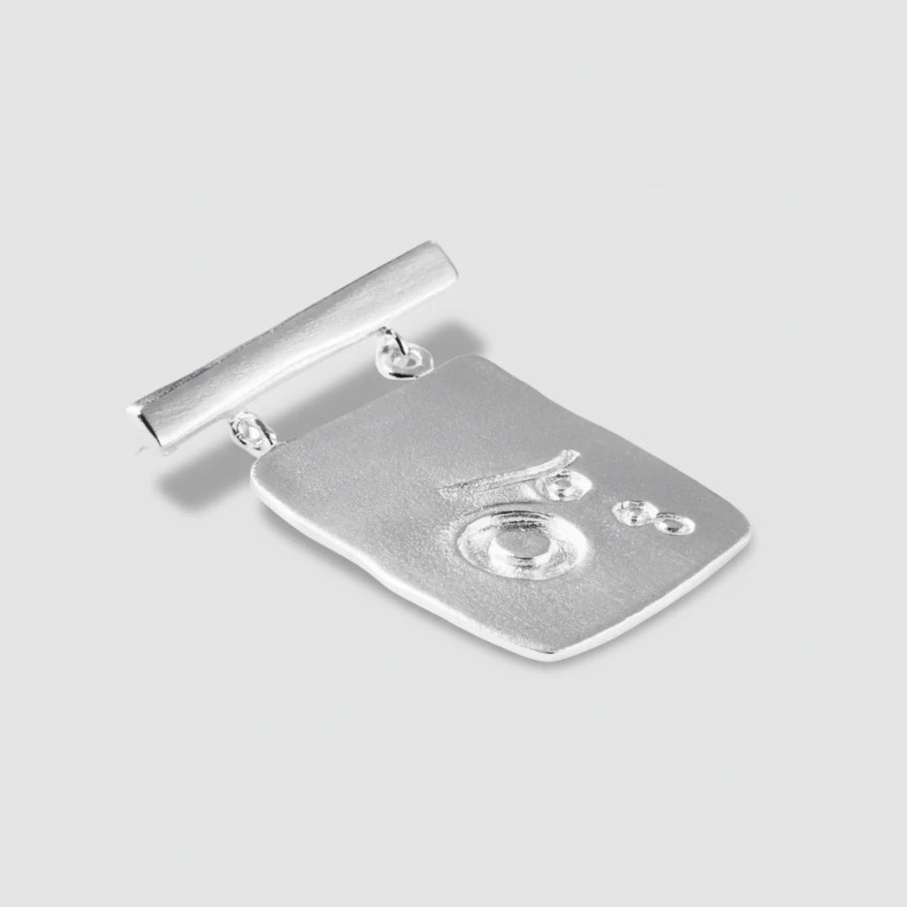 Silver brooch with a detailed design on a white background