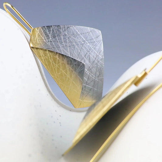 Gold and silver leaf-shaped earrings on a light background