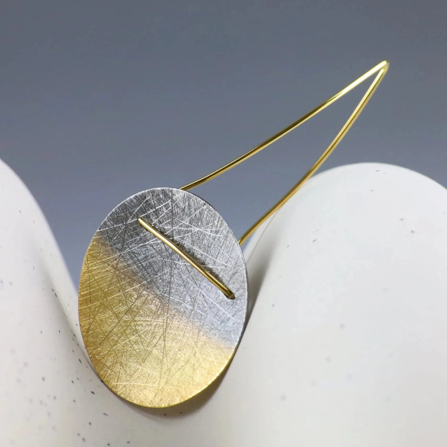 Gold and silver earring on a white surface with a gray background