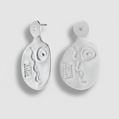 Pair of silver earrings with abstract designs on a light gray background