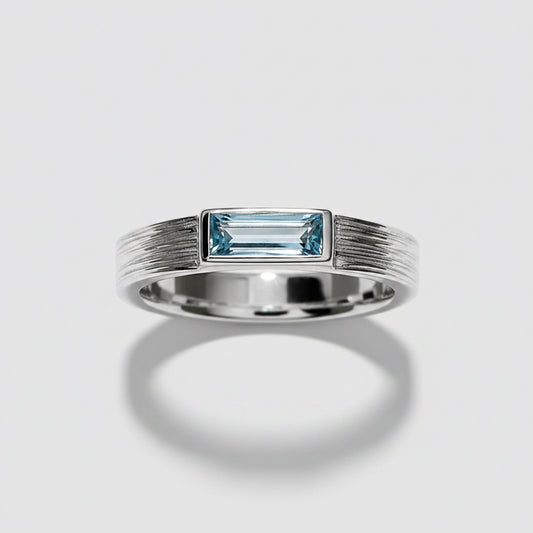 A silver band ring featuring a rectangular baguette-cut light blue gemstone in a bezel setting, with a textured, ribbed design on the shoulders, shown on a white background