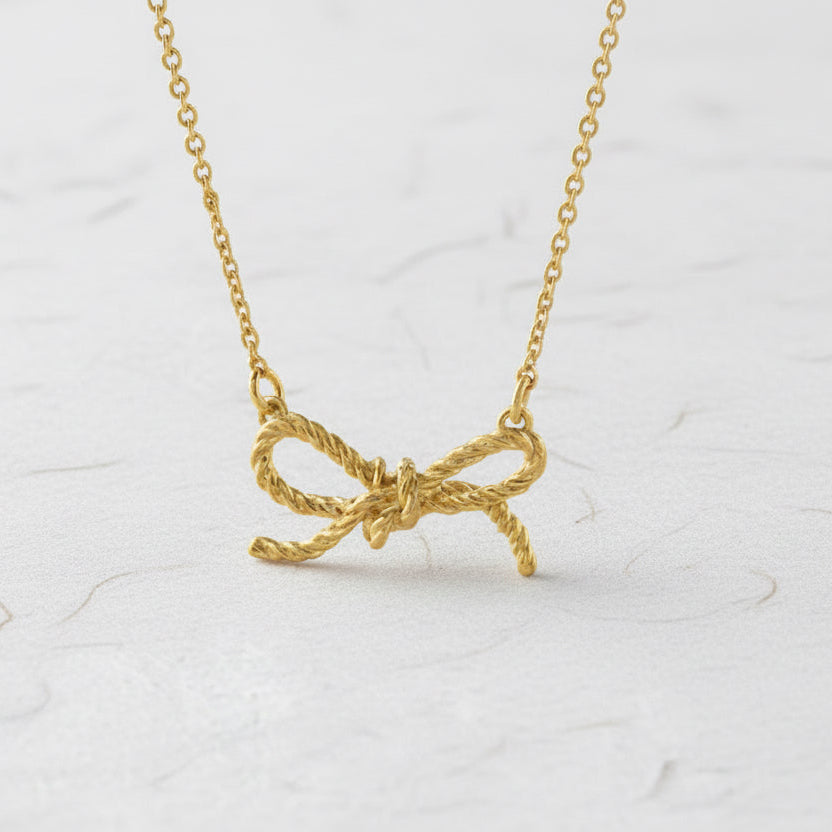 Gold bow-shaped pendant on a chain against a white background